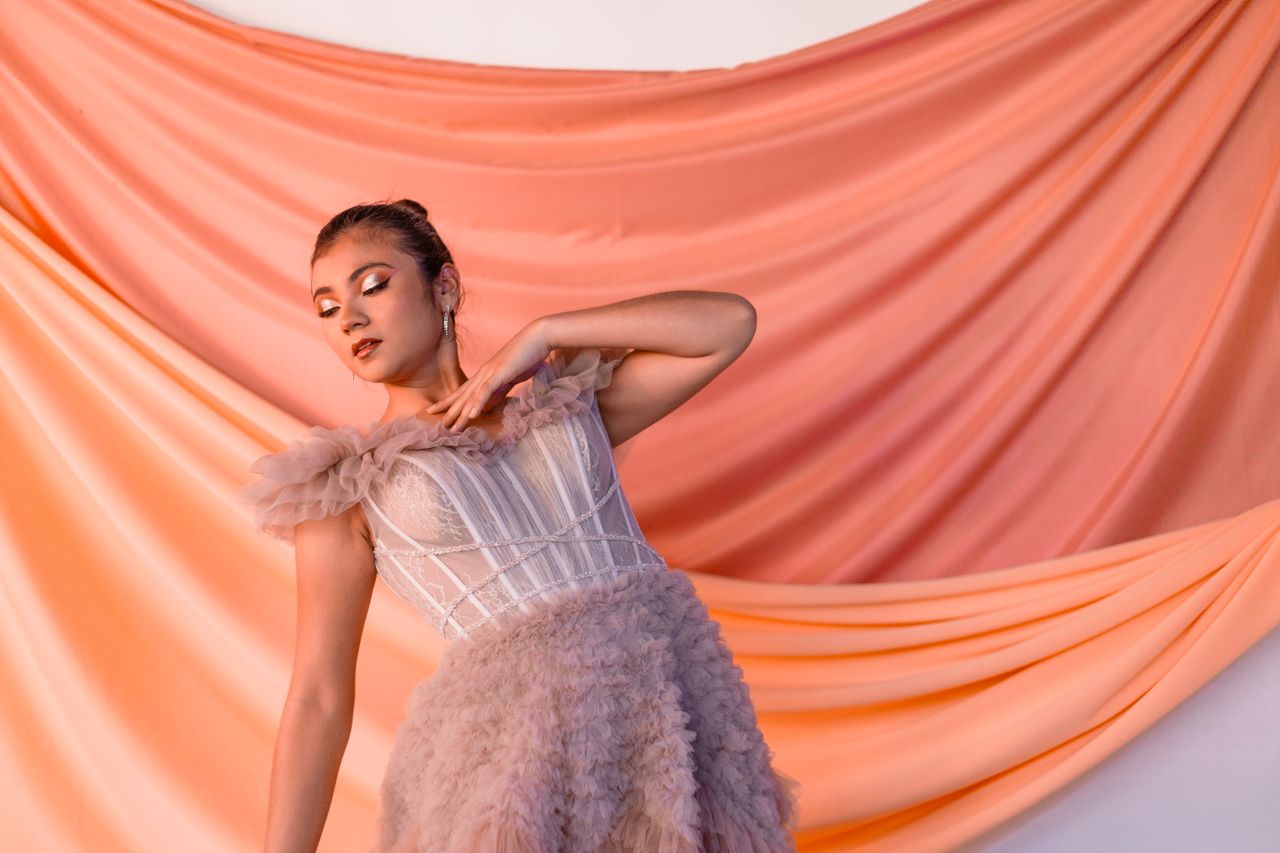 Portrait of a woman in a delicate dress against peach drapery, exuding elegance.