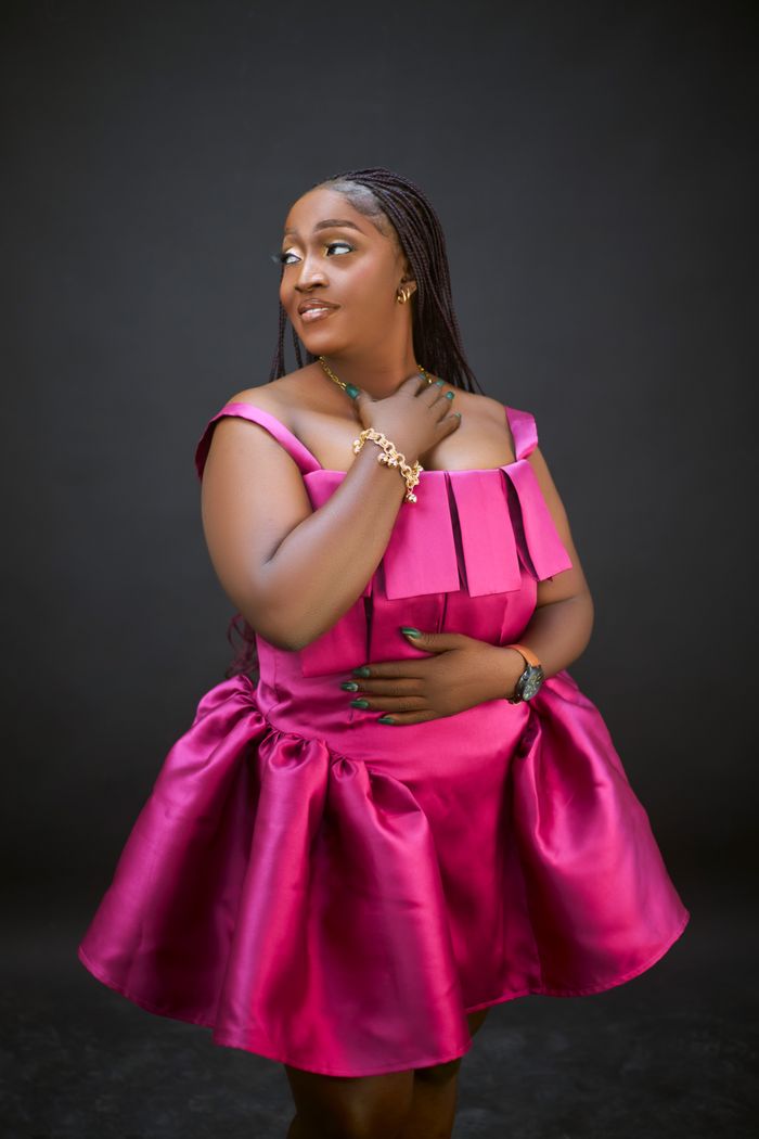 Confident woman posing in a stylish pink dress against dark background.