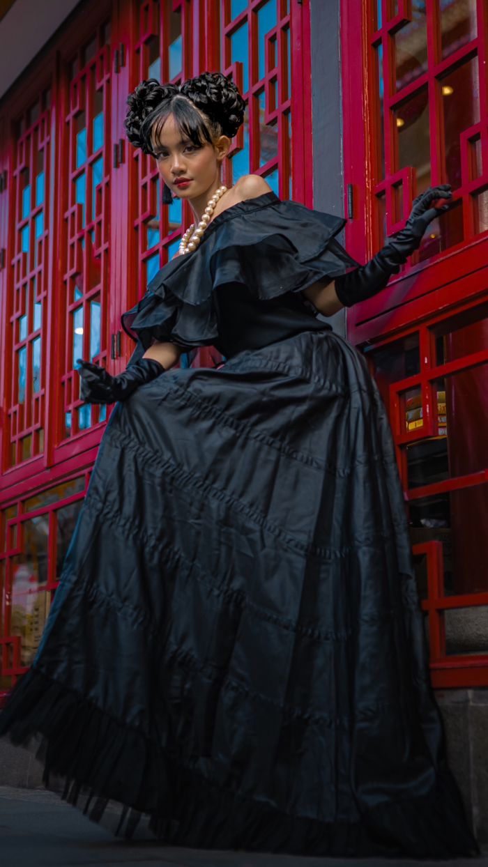 mission-02 Stylish portrait of a woman in an elegant black dress in front of red Chinese architecture.